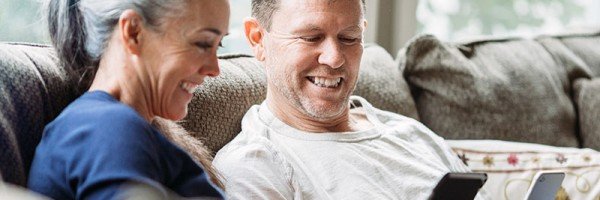 Older couple sat at home on a sofa smiling
