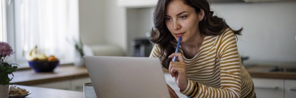 Woman stood at kitchen counter with laptop comparing savings accounts