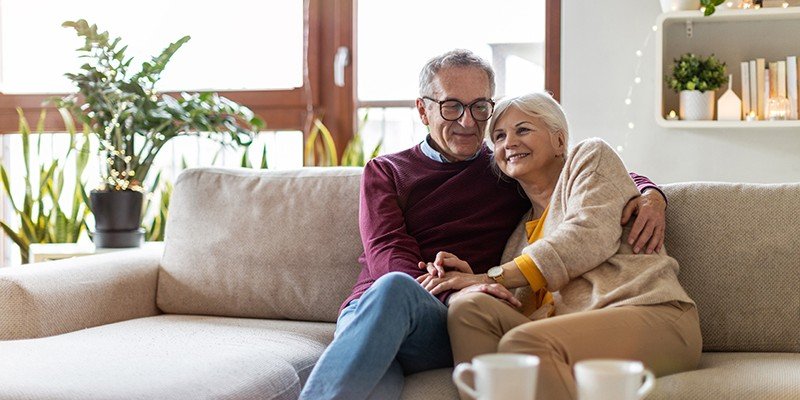 Older couple sat on sofa smiling